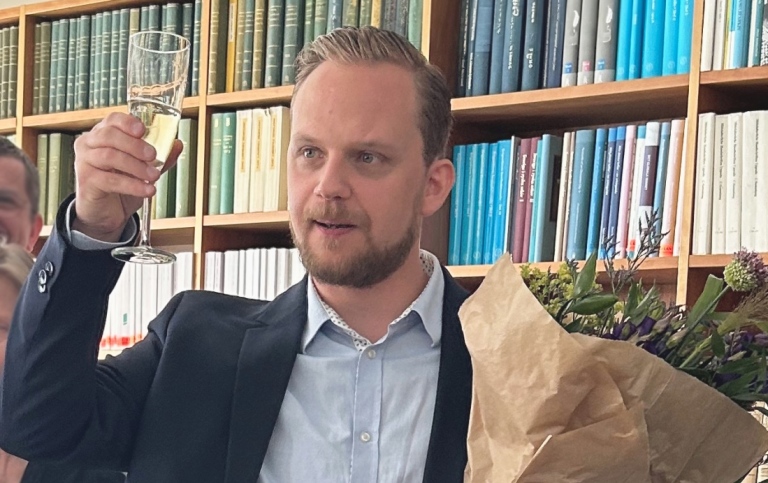 En person står med ett glas och skålar med en blombukett i hand.